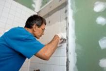 a handyman installs new tile in a tub enclosure